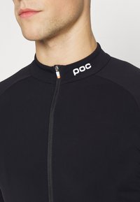 Maillot de cyclisme noir avec un col zippé, arborant un logo "poc" blanc et une tirette de zip orange. Fabriqué dans un tissu lisse et extensible.