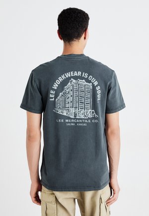 T-shirt in cotone grigio scuro a maniche corte, con una grande grafica bianca di un edificio e del testo sul retro. Vestibilità rilassata.