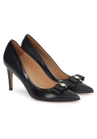Scarpe col tacco alto in pelle nera con punta affusolata, dettaglio a fiocco e hardware dorato sulla parte anteriore, tacchi a spillo sottili, texture liscia.