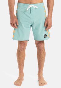 Svetlo modré plavky s plochým pásom a bielym šnúrkovým viazaním. Na stranách sú zvýraznené oranžové kostkované akcenty. Rýchloschnúca látka.