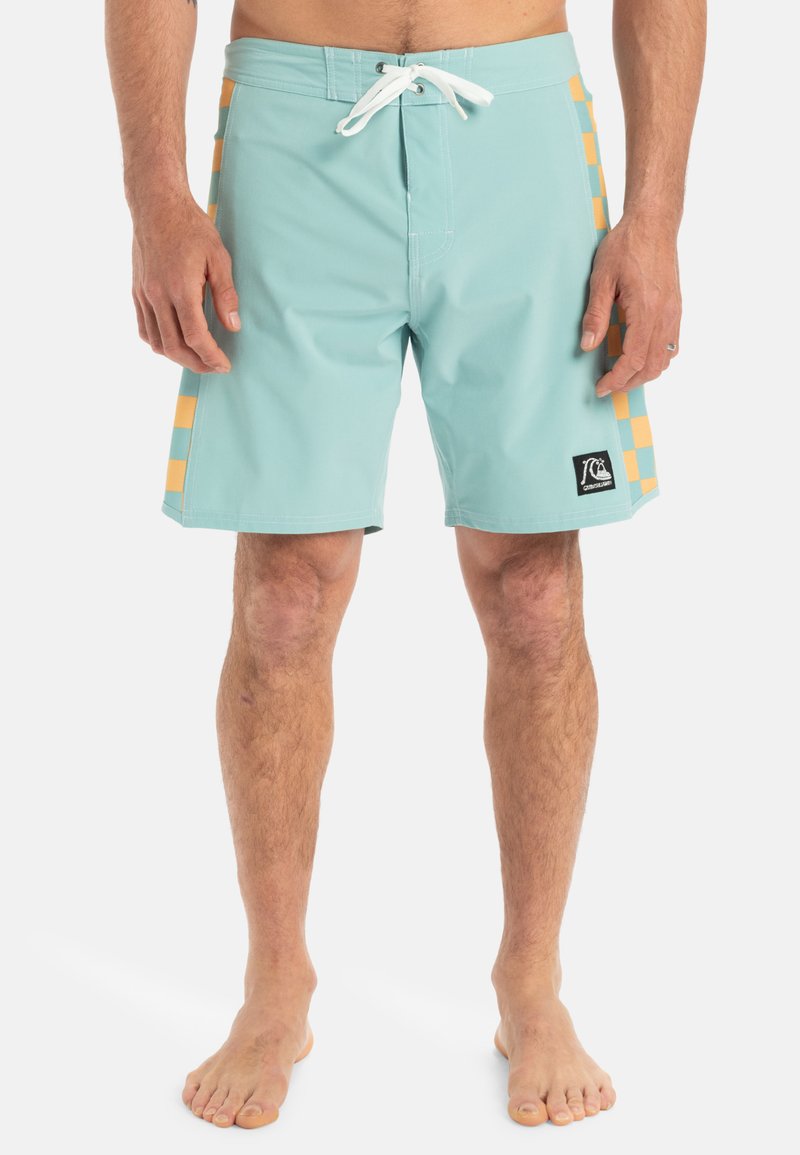 Svetlo modré plavky s plochým pásom a bielym šnúrkovým viazaním. Na stranách sú zvýraznené oranžové kostkované akcenty. Rýchloschnúca látka.