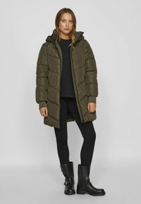 Olīvu zaļš pūkainais mētējs ar rāvējslēdzēja aizdari un kapuci, ar izsistiem rakstiem un ribotām piedurknēm. Valkāts ar melnu augšu un šaurām biksēm. Melni zābaki.