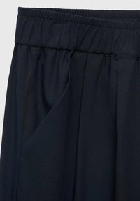 Marineblauwe, lichtgewicht stofbroek met een elastische tailleband, voorzien van zijzakken en een zachte, gladde textuur met subtiele plooien.