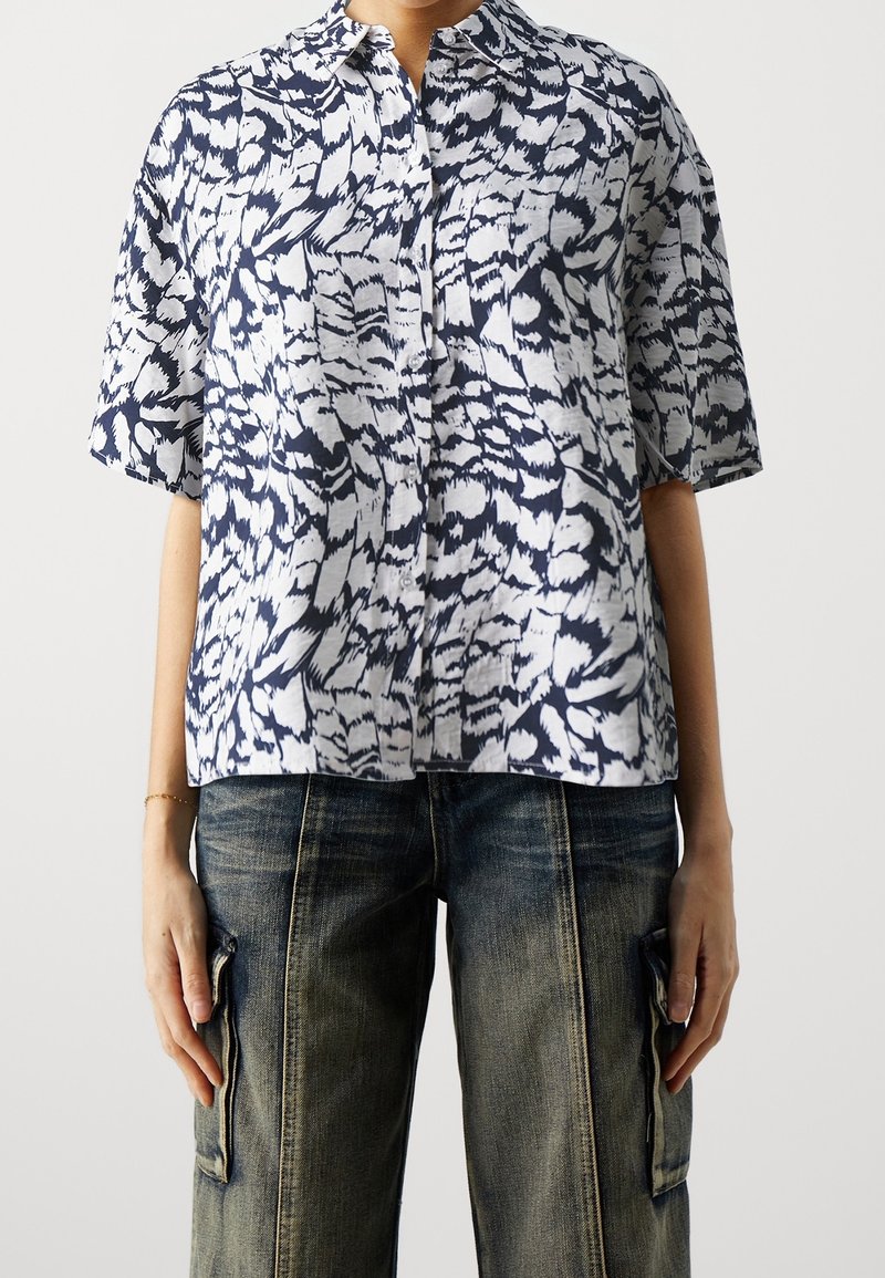 Camicia a maniche corte, con bottoni, in tessuto a fantasia blu e bianca, caratterizzata da una vestibilità rilassata e una texture morbida, abbinata a pantaloni cargo in denim scuro.