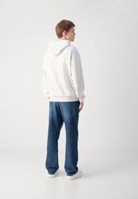 Sudadera blanca con capucha de corte relajado, combinada con unos vaqueros de denim azul holgados. Diseño sencillo, textura suave y mínima visibilidad de la marca.