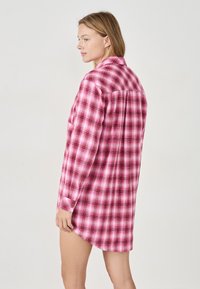 Różowa koszula w kratę z długim rękawem, z kołnierzykiem zapinanym na guziki i zaokrąglonym dołem. Charakteryzuje się miękką fakturą oraz kontrastowym wzorem w białe i ciemnoróżowe kratki.