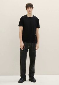 Sort T-shirt med korte ærmer og rund halsudskæring, kombineret med sorte jeans med synlige hvide syninger og sorte snøresko.