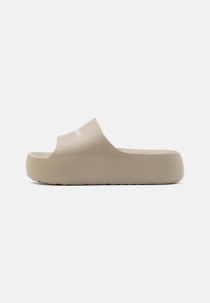 Beige slip-on sandal med tyk sål, åben tå og bred rem over toppen med lille hvid branding