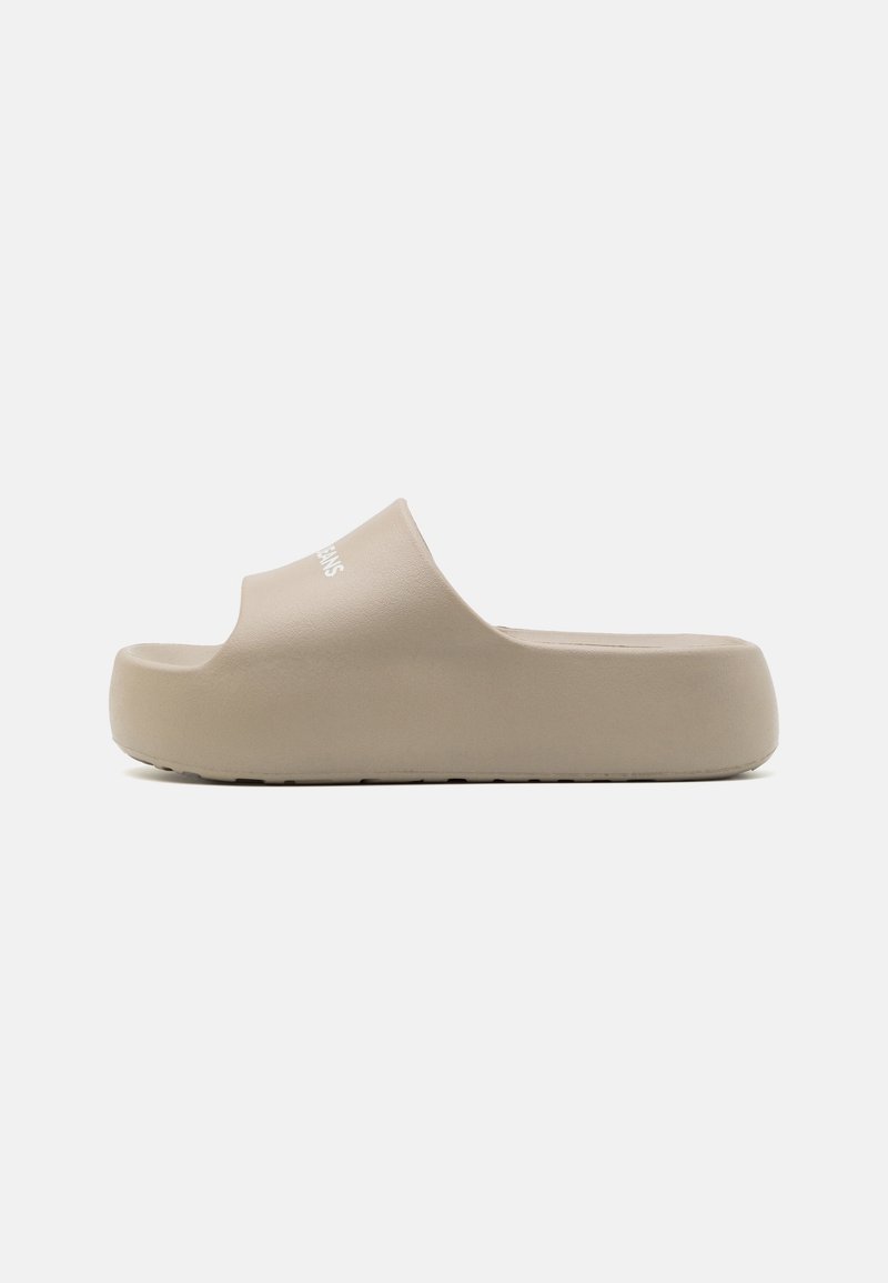Sandale beige à enfiler avec une semelle épaisse, orteil ouvert et large bride sur le dessus avec petit marquage blanc