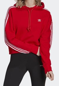 Red cropped hoodie made of cotton blend, featuring white three-stripe design along sleeves and an embroidered logo on the chest.