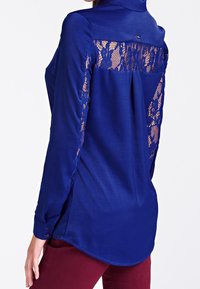 Chemise bleu marine à manches longues, avec des panneaux en dentelle transparente aux épaules et dans le dos, des poignets à boutons et un ourlet arrondi. Texture de tissu lisse.