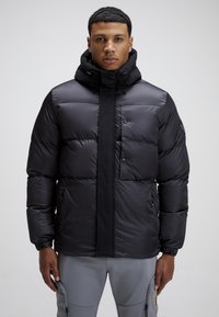 Giacca a vento nera con colletto alto, chiusura a zip e bottone, e polsini elasticizzati. Presenta una texture liscia e sofisticata e più tasche.
