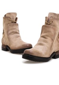 Beżowe zamszowe botki za kostkę o lekko pomarszczonej powierzchni, okrągłym nosku, niskim obcasie i dekoracyjnych złotych elementach po bokach.