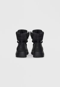 Black ankle boots featuring a padded upper, textured synthetic material, two side zippers, and a thick rubber sole with a branded heel.