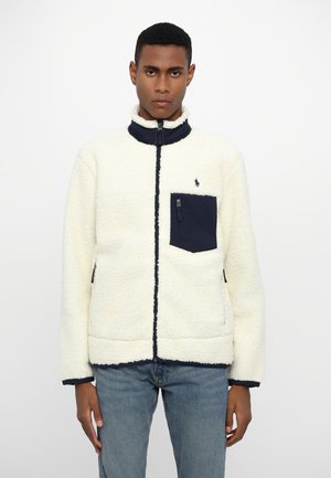 Fleece jacket in ivory with a navy collar and pocket. Features zip pocket and contrasting stitching. Soft texture and relaxed fit.