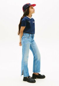 T-shirt navy con colletto bianco, jeans blu chiaro con fessure laterali e mocassini neri. Un cappellino da baseball rosso e navy completa il look.