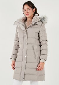 Svijetlosiva puffer jakna s odvojivom kapom obloženom krznom, kviltani dizajn, bočni zatvarači i rebrasti manžeti za dodatnu toplinu.