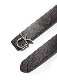 Sort læderbælte med præget mønster og spænde i sølvmetal med "CK" logo. Strappen har tekstureret detaljer over hele overfladen; spids afslutning.