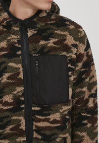 Fleece jacket in green, brown, and tan camouflage pattern with a black zippered chest pocket and front zipper. Features a hood.