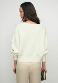 Krémový, oversized svetr s žebrovaným lemem a širokými rukávy. Hladká textura, pletená tkanina. Spárováno s světle béžovými kalhotami.