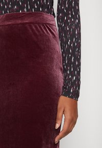 Falda de terciopelo burdeos con una textura suave y cinturilla, combinada con una blusa negra de manga larga con un patrón abstracto multicolor.