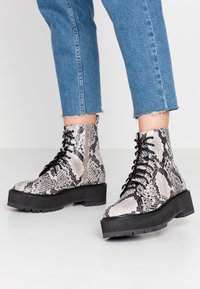 Botas de caña baja con cordones y suelas de plataforma negra, con un patrón de piel de serpiente, combinadas con unos vaqueros azules recortados.