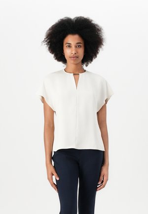 Lichtbeige top met een sleufhals, korte mouwen en een gladde textuur. Gepaard met donkerblauwe broeken, waardoor een contrasterende ensemble ontstaat.
