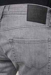 Jeans de mezclilla gris con una textura suave, que cuentan con bolsillos traseros, costuras en contraste y un parche de cuero negro de la marca en la cinturilla.