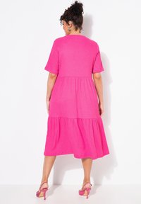 Fuksia midi-mekko lyhyillä hihoilla, kerroksellinen muotoilu, pehmeä rakenne ja rento istuvuus. Yhdistetty vaaleanpunaisiin korkokenkiin.