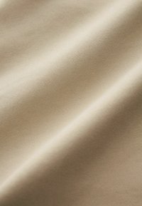 Beige pamut anyag sima textúrával, diszkrét átlós bordázattal és enyhe fénylő hatással, lágyan hullámzó redőkben omlik.