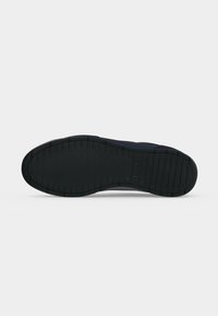 Semelle en caoutchouc noire d'une chaussure avec des lignes horizontales de la bande de roulement et le logo "BOSS" embossé près du talon sur un fond clair uni.
