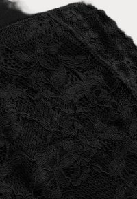 Zwarte kanten stof met bloemen- en bladmotieven, met gegolfde randen en doorschijnende mesh-gebieden.