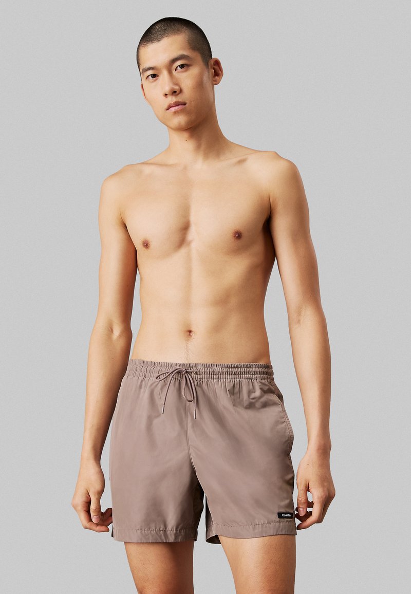 Pantaloni da mare da uomo realizzati in tessuto leggero e ad asciugatura rapida, di colore marrone tenue, con cintura elastica e tasche laterali.