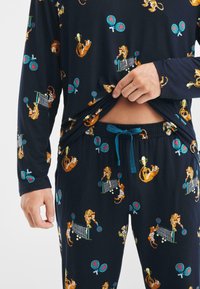 Conjunto de pijama azul marino que incluye una camiseta de manga larga y pantalones con cinturilla elástica, decorado con coloridos gráficos de tigres y tenis. Textura de material suave.