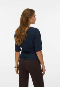 Marineblå kortærmet top lavet af blødt stof med afslappet pasform og rundet kant, kombineret med mørkebrune bukser.