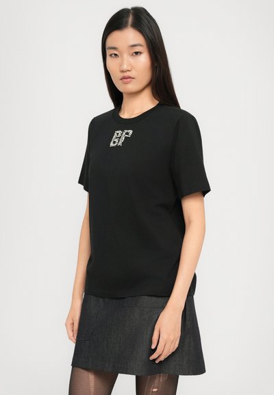Μαύρη κοντομάνικη μπλούζα φτιαγμένη από βαμβάκι, με ένα λαμπερό σχέδιο "BF" στο στήθος. Συνδυάζεται με μια σκούρα τζιν φούστα.