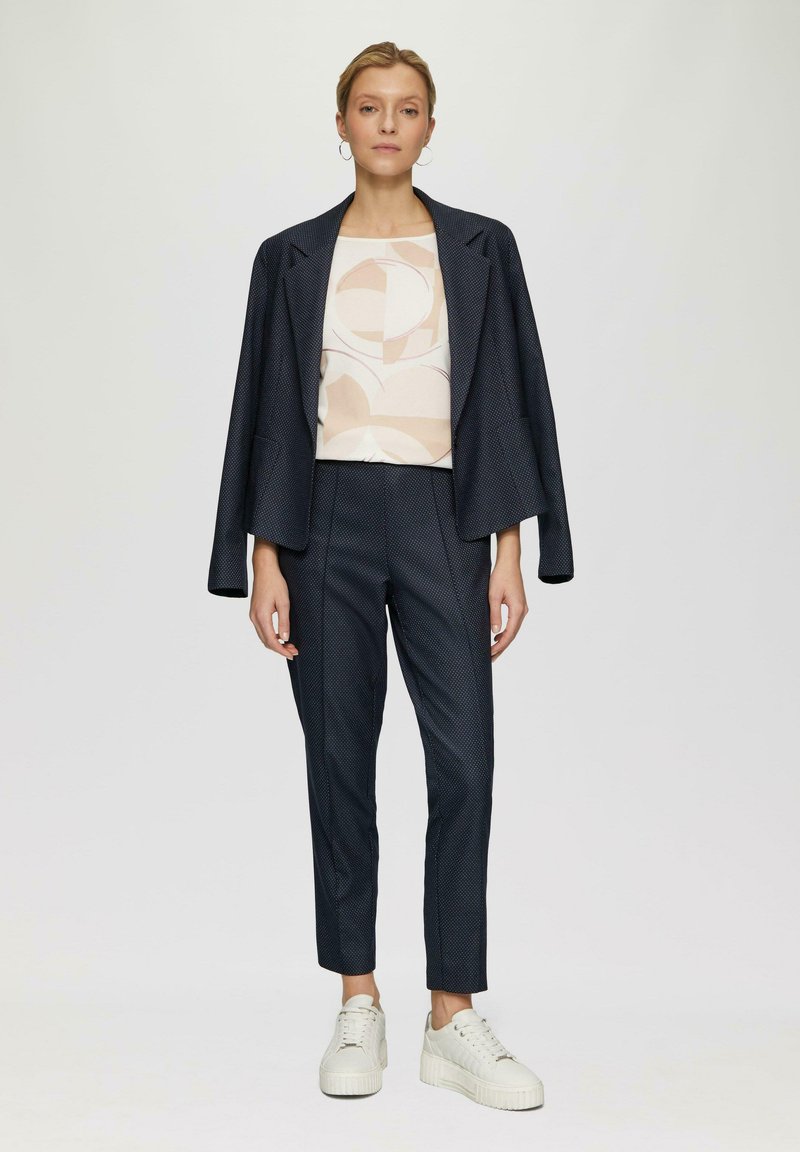 Marineblazer met een gestructureerd ontwerp, gecombineerd met een gestreept licht shirt en slim-fit marineblauwe broek. Schoenen zijn witte sneakers met dikke zolen.