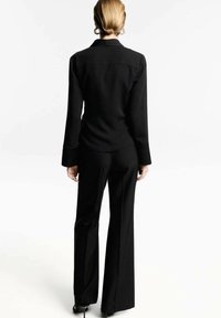 Haut noir à manches longues, coupe droite avec un col discret, assorti à un pantalon taille haute à jambes larges.