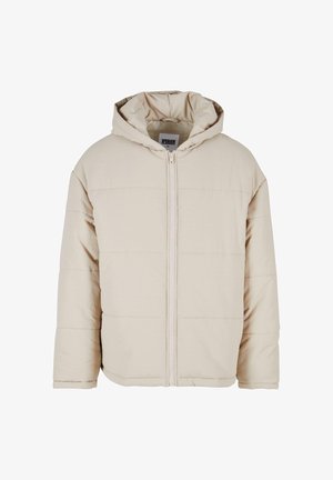 Bēšas krāsas kapuces pūkainā jaka ar priekšējo rāvējslēdzēju, quiltēto rakstu un brīvu piegriezumu. Izgatavota no mīksta materiāla, ar elastīgiem piedurkņu galiem.