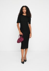 Vestido midi preto de malha com mangas curtas bufantes, combinado com uma bolsa de mão burgundy e sapatos de salto alto pretos. Textura suave e design ajustado.