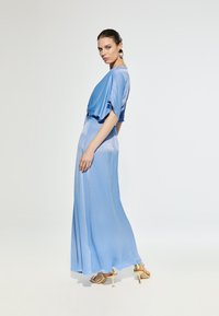 Svijetloplava satenasta maksi haljina s kratkim, labavim rukavima i lepršavom suknjom, uparen s zlatnim sandalama na visoku petu i okruglim naušnicama.