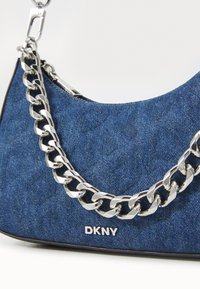 Kék farmer táska ívelt formával, ezüst láncos fogantyúval és az elülső részen "DKNY" márkájú logóval. Texturált kék anyag kontrasztos részletekkel.