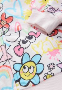 Weißer Baumwollstoff mit bunten Cartoon-Drucken, einschließlich Blumen, Herzen und verspielten Gesichtern. Rippbündchen in sanftem Rosa.
