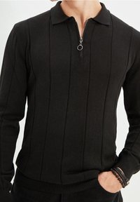 Polo nero a maglia con maniche lunghe e zip a un quarto, caratterizzato da pannelli a coste verticali e una finitura testurizzata. Polsini e vita morbidi e aderenti.