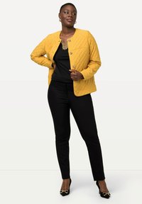 Quiltet gul jakke med rund hals og knaplukninger, parret med sort top og skræddersyede bukser, akkompagneret af guld sko.