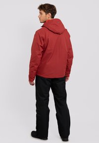Chaqueta impermeable roja con capucha, pantalones cálidos negros y calzado negro; textura suave con forro interior en contraste y adecuado para uso al aire libre.