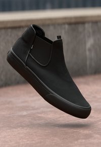 Botas negras de tobillo con un acabado de ante suave, paneles laterales elásticos y una suela de goma texturizada. Diseño elegante con acentos mínimos.