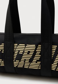 Μαύρη τσάντα tote με γραφικό σχέδιο με κίτρινες ρίγες, εξοπλισμένη με ανθεκτικές χειρολαβές και κλείσιμο με φερμουάρ, κατασκευασμένη από ανθεκτικό υλικό.