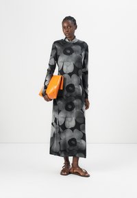 Long black dress with large gray floral patterns, long sleeves, and a high neckline. Holding an orange leather bag. Brown strappy sandals.