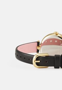 Correa de reloj de cuero negro con un hebilla de metal dorado, con un interior rosa y una esfera de reloj redonda y transparente.